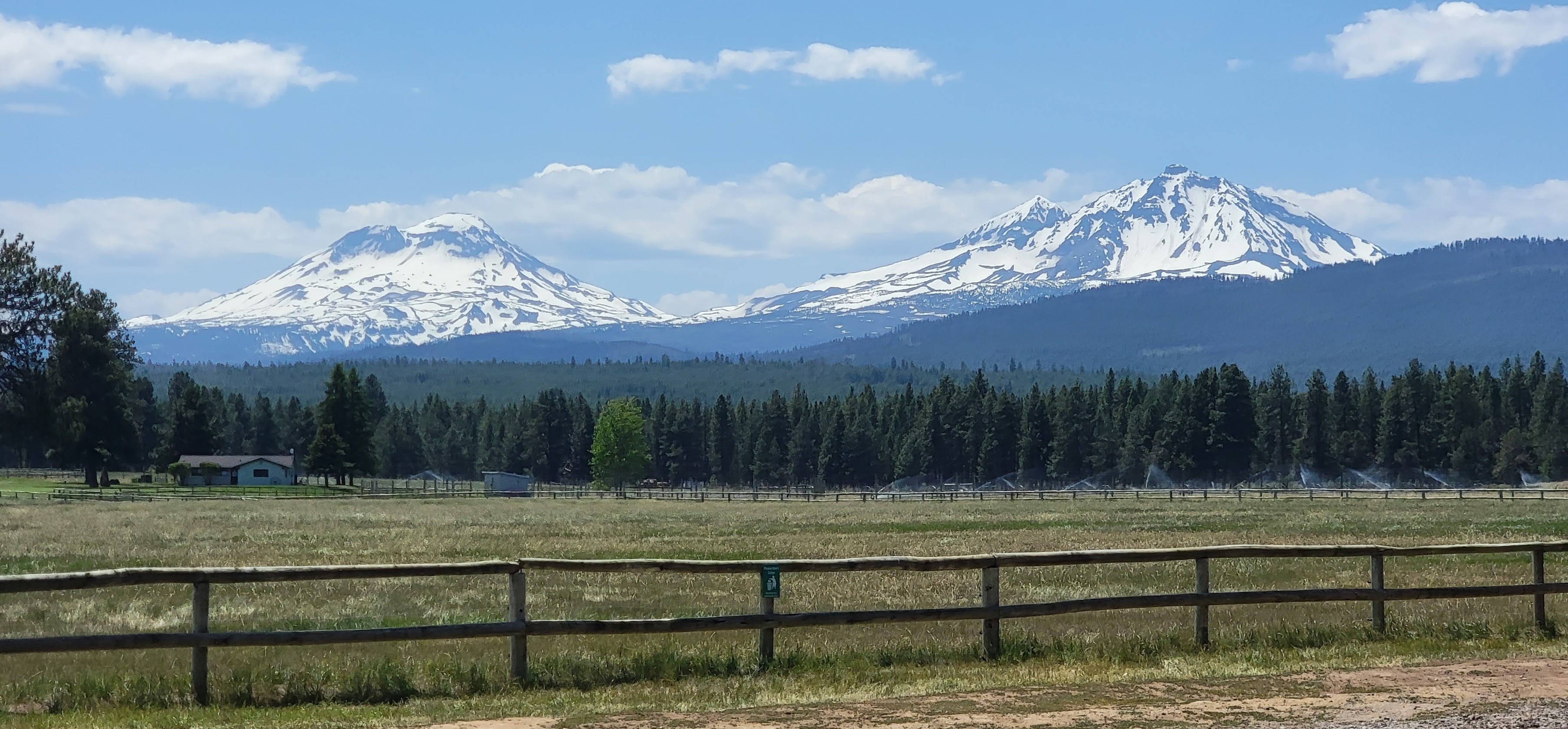 Beautiful scene featuring a wooden fence, a green pasture, and the sisters mountains in the background